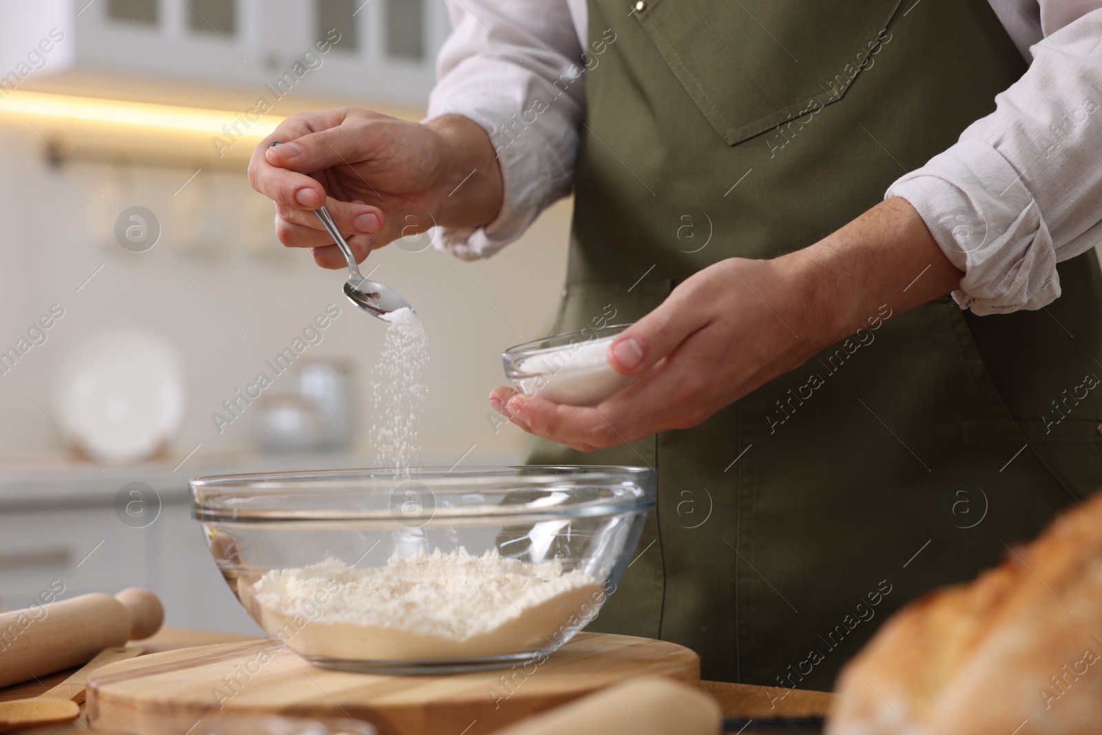 Photo of Making bread. Man putting salt into bowl with flour at wooden table in kitchen, closeup