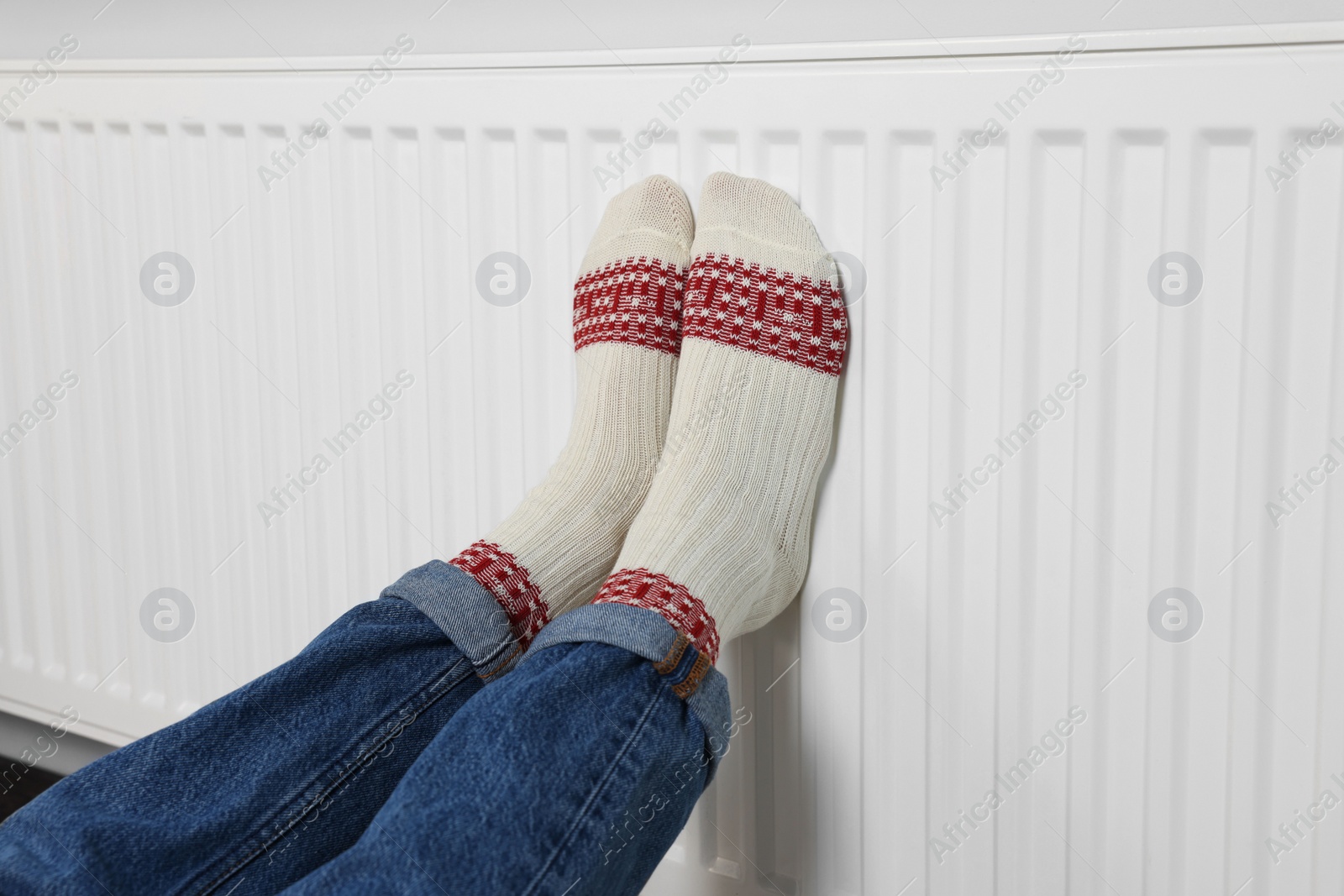 Photo of Woman warming legs on heating radiator near white wall, closeup