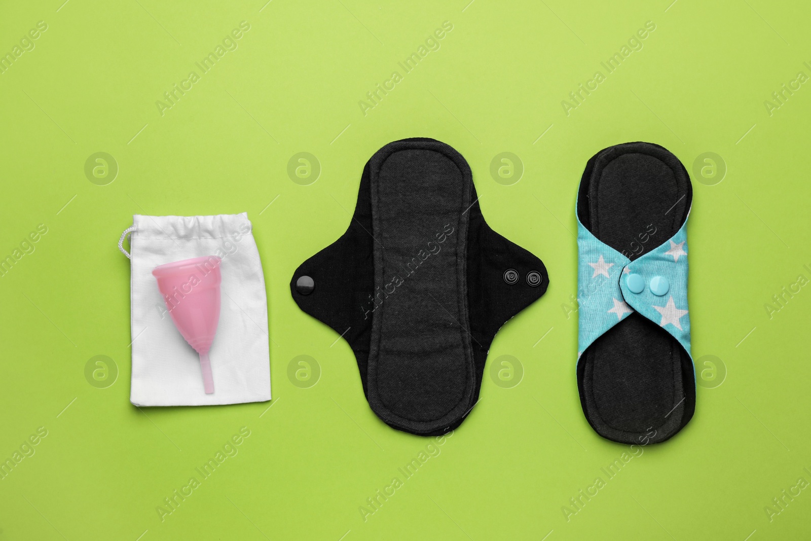 Photo of Reusable cloth pads and menstrual cup on green background, flat lay