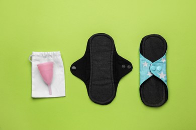 Photo of Reusable cloth pads and menstrual cup on green background, flat lay