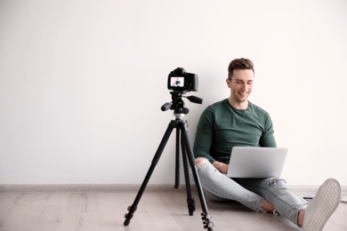 Young blogger with laptop recording video near light wall