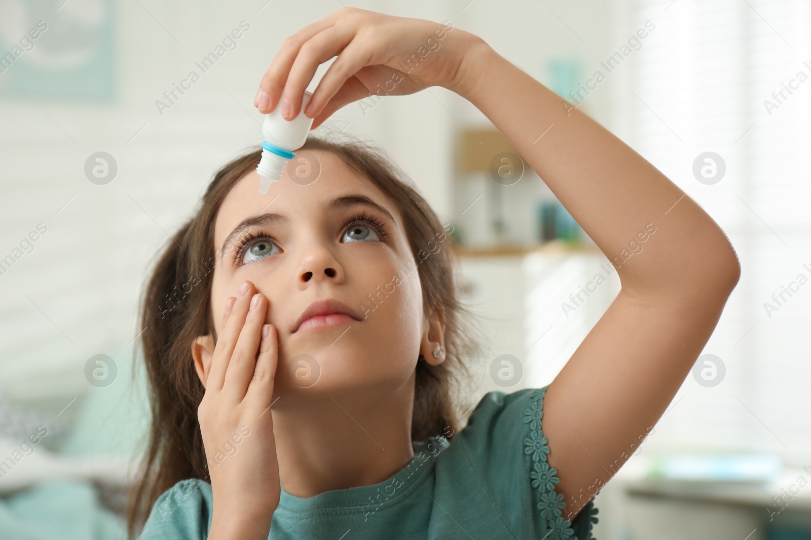 Photo of Adorable little girl using eye drops indoors