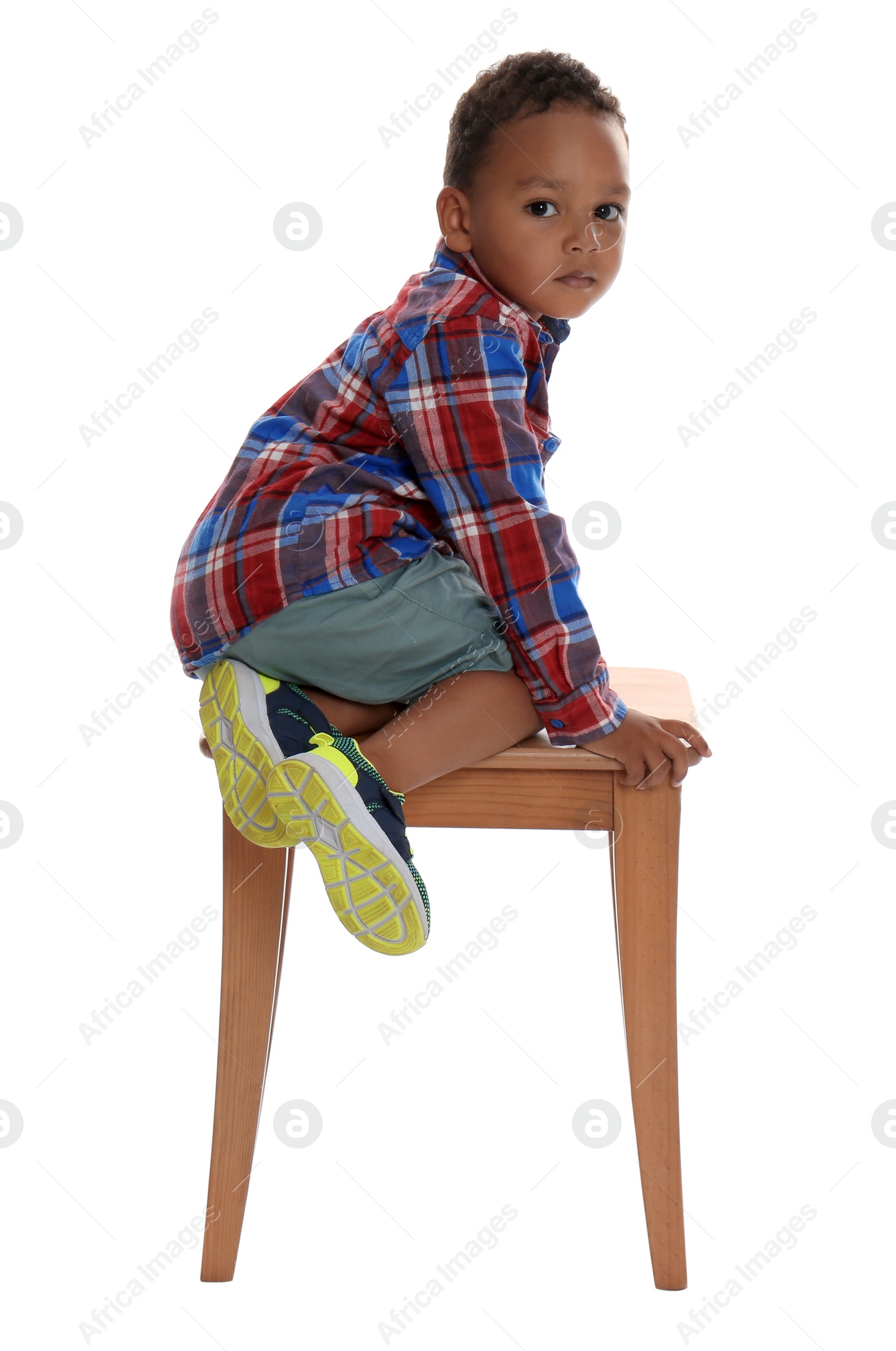 Photo of Little African-American boy climbing up stool on white background. Danger at home