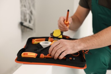 Photo of Electrician taking screwdriver from tool bag indoors, closeup