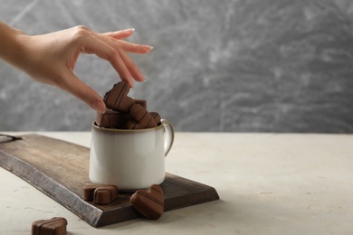 Photo of Woman taking heart shaped chocolate candy from cup at light table, closeup. Space for text