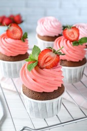 Delicious cupcakes with cream and strawberries on white table, closeup