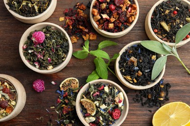 Photo of Different kinds of dry herbal tea in bowls on wooden table, flat lay