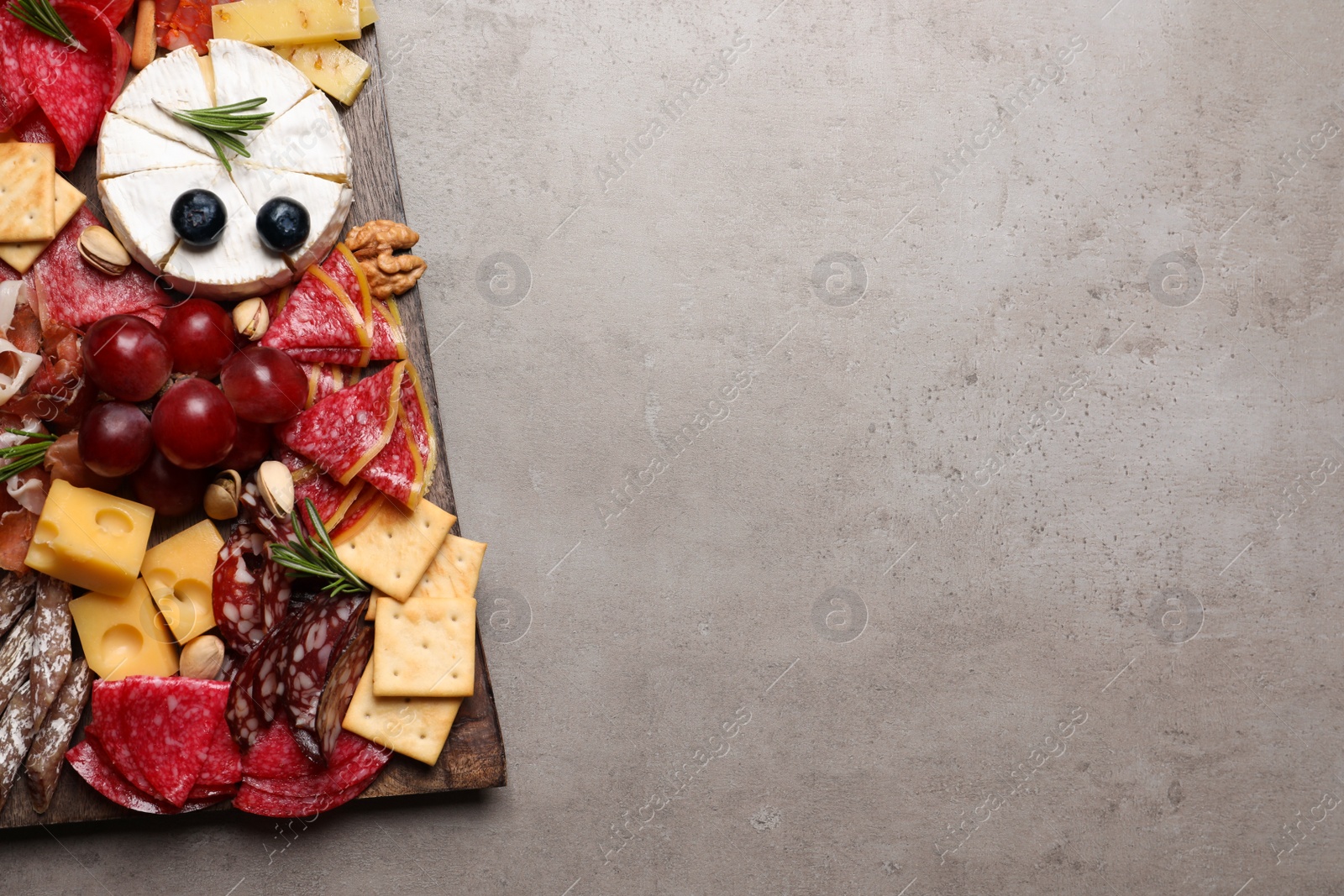 Photo of Wooden board with different appetizers on grey table, top view. Space for text