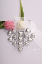 Photo of Heart made with delicious chocolate candies and beautiful tulips on white background, top view