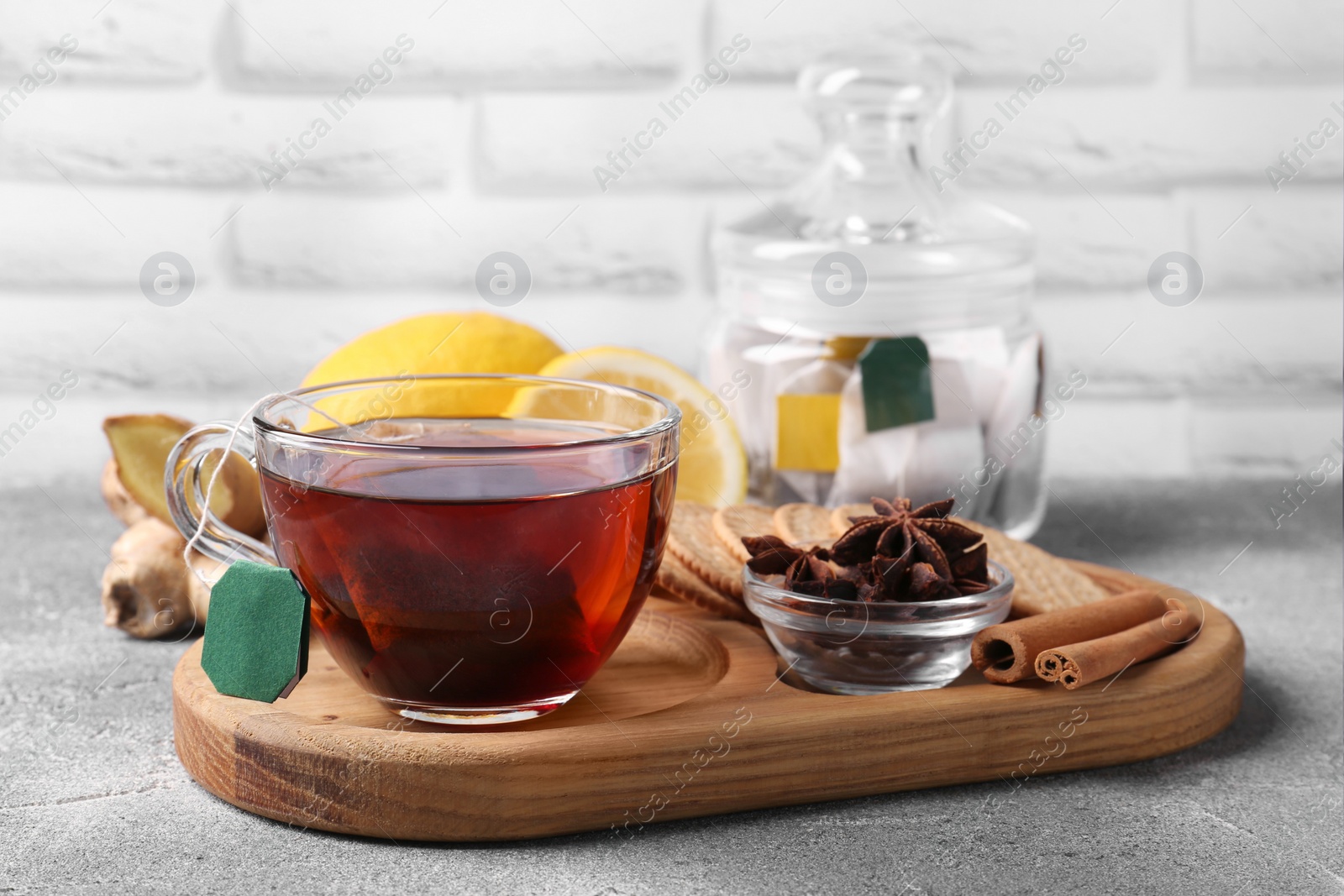 Photo of Tea bag in glass cup, anise stars, cinnamon sticks and cookies on light grey table