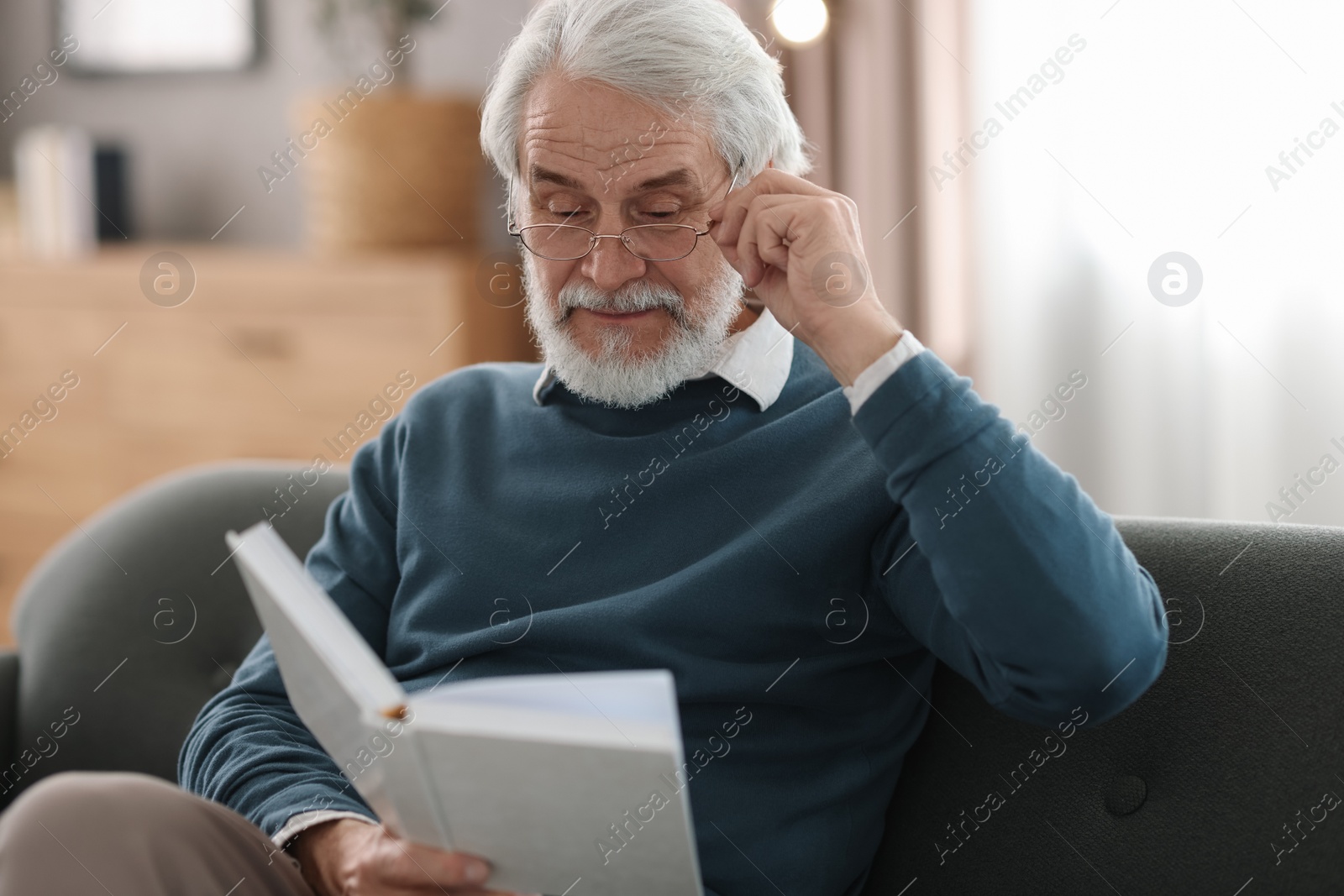 Photo of Portrait of happy grandpa reading book on sofa indoors