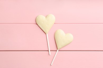 Chocolate heart shaped lollipops on pink wooden table, flat lay