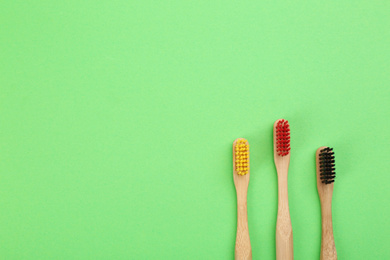Photo of Natural toothbrushes made with bamboo on green background, flat lay. Space for text
