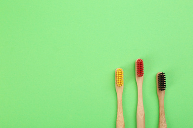 Natural toothbrushes made with bamboo on green background, flat lay. Space for text