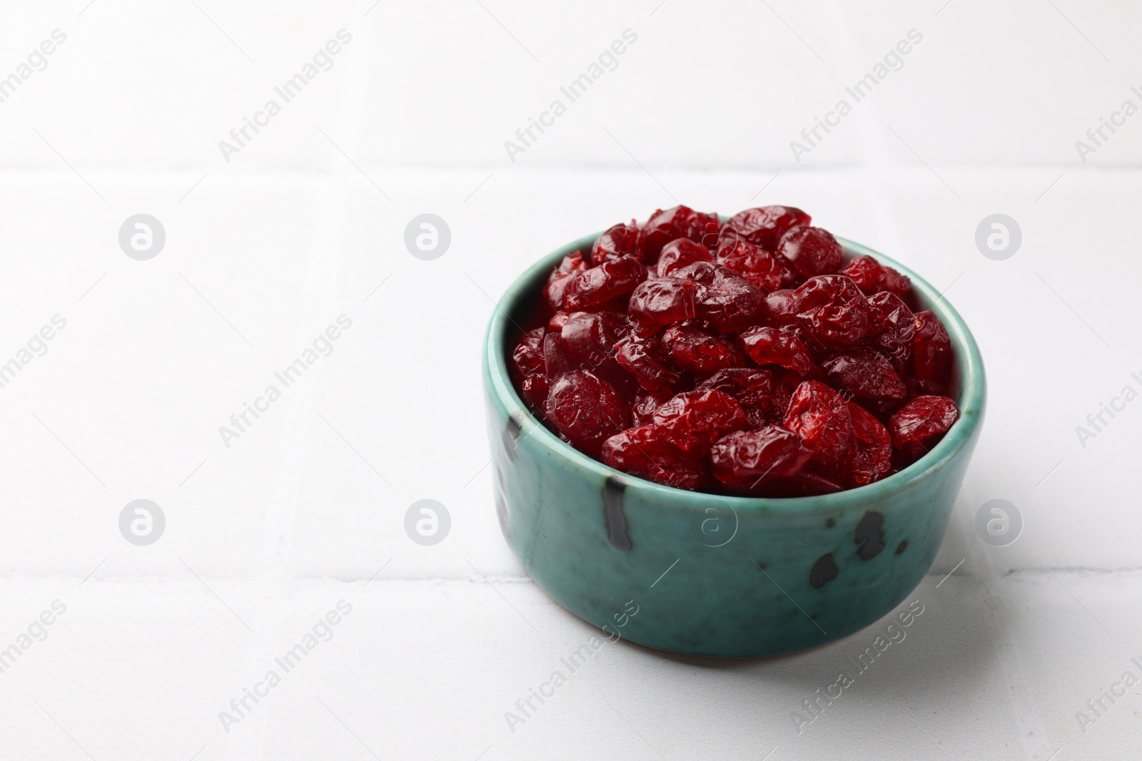 Photo of Tasty dried cranberries in bowl on white tiled table. Space for text