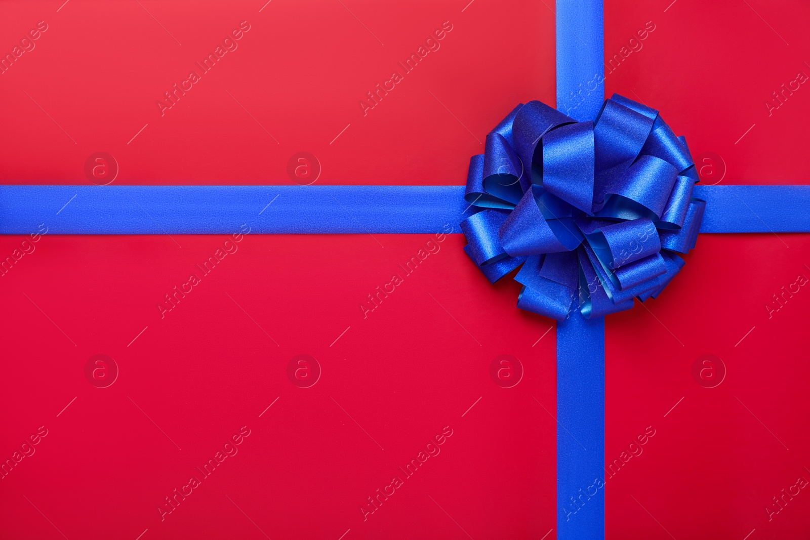 Photo of Blue ribbons with bow on red background, top view