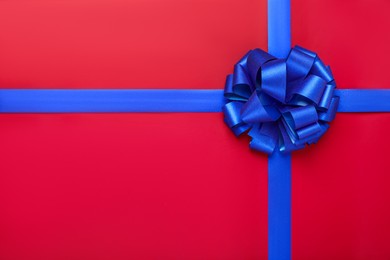 Photo of Blue ribbons with bow on red background, top view