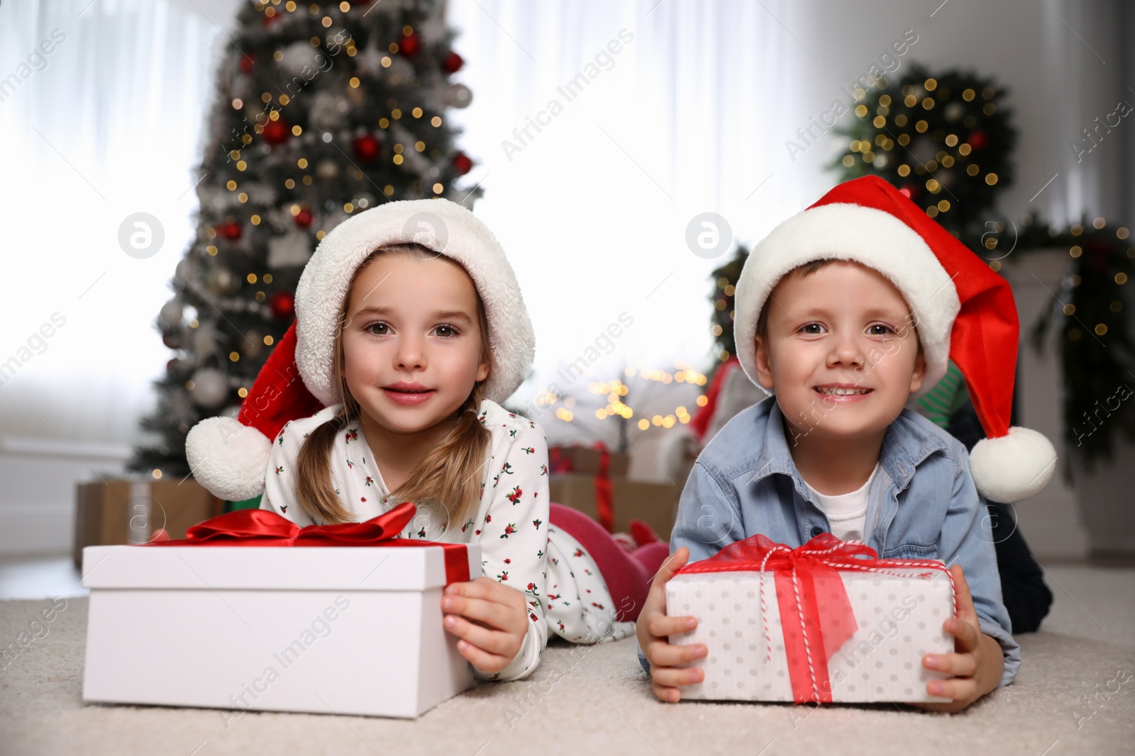Photo of Cute little children with Christmas gifts on floor at home