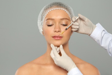 Photo of Young woman getting lips injection on grey background. Cosmetic surgery