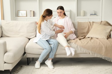 Doula taking care of pregnant woman on sofa at home. Preparation for child birth