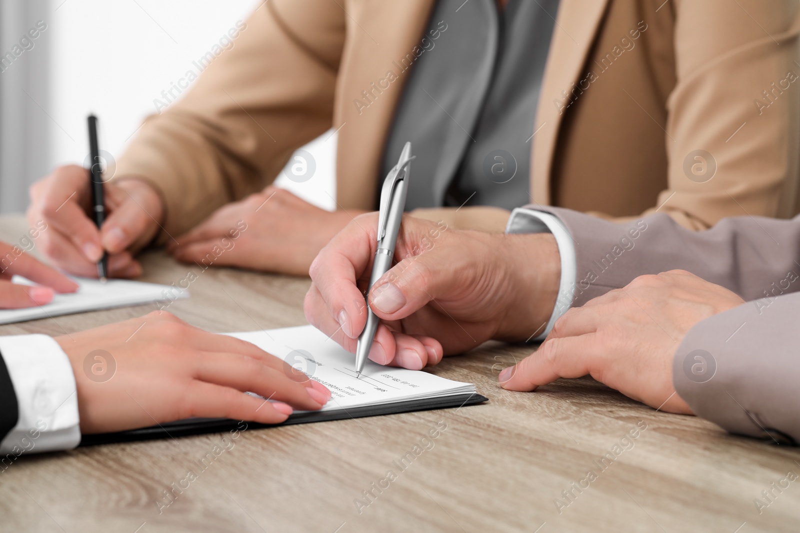 Photo of Manager showing client where he must to mark signature at light wooden table indoors, closeup