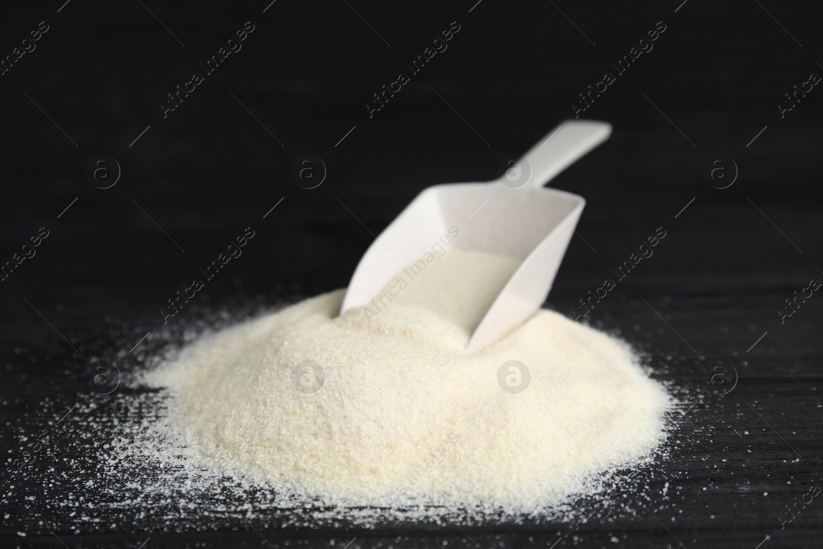 Photo of Pile of gelatin powder and scoop on black wooden table