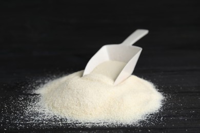 Photo of Pile of gelatin powder and scoop on black wooden table