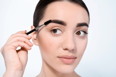 Photo of Beautiful woman with perfect eyebrows applying makeup on light background
