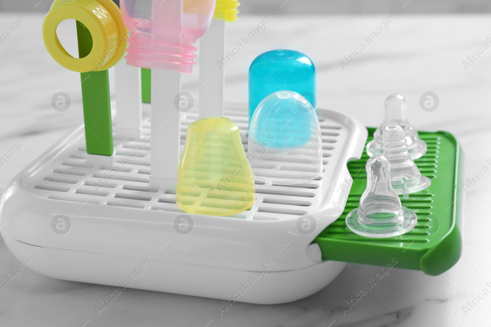 Photo of Dryer with baby bottles and nipples after sterilization on white marble table in kitchen, closeup