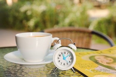 Photo of Cup of drink, alarm clock and magazine on table  outdoors in morning
