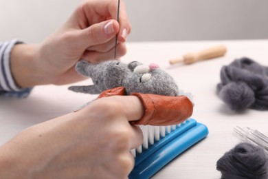 Photo of Woman felting toy cat from wool at light table, closeup