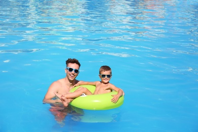 Little boy on inflatable ring with happy father in swimming pool