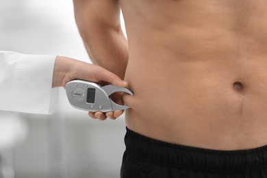 Photo of Nutritionist measuring man's body fat layer with digital caliper on blurred background, closeup