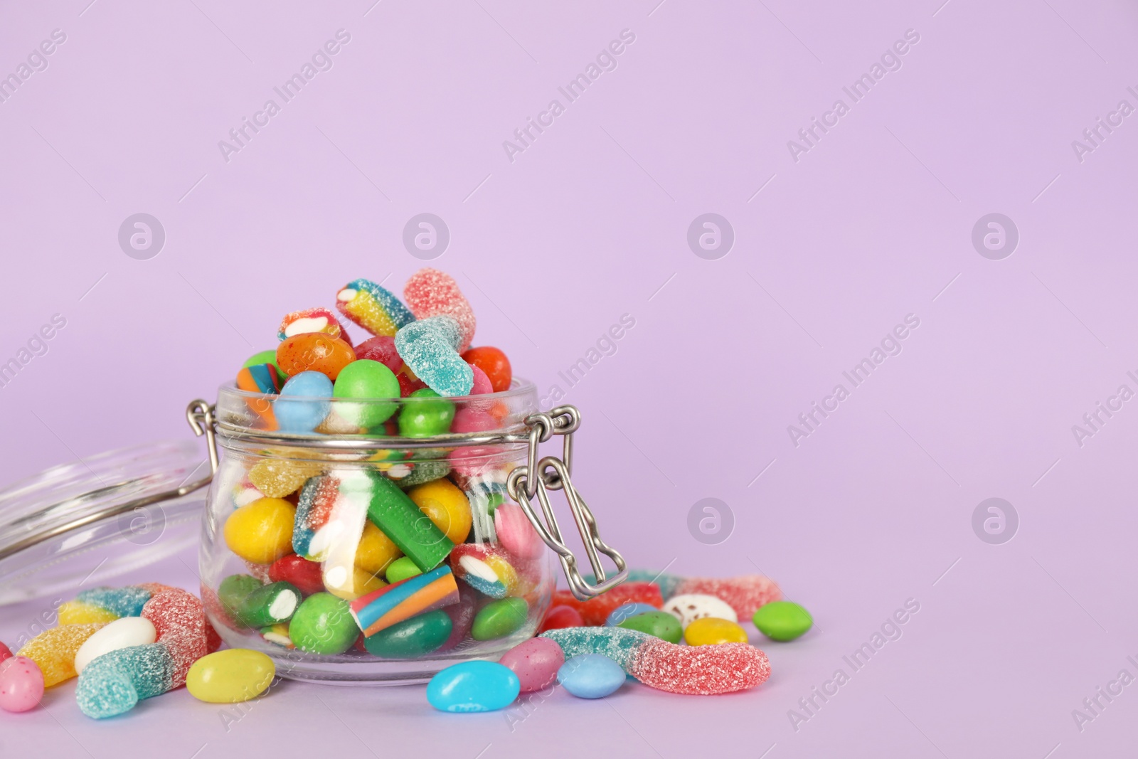 Photo of Glass jar with different candies on pale violet background, space for text