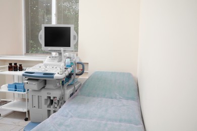 Photo of Ultrasound machine, medical trolley and examination table in hospital. Space for text