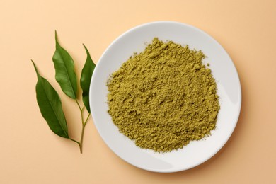 Henna powder and green leaves on beige background, flat lay. Natural hair coloring