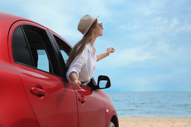 Photo of Happy woman leaning out of car window on beach. Summer vacation trip