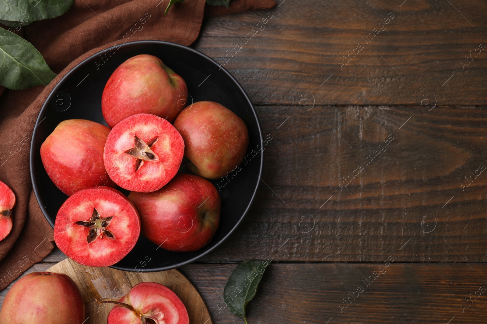 Photo of Tasty apples with red pulp and leaves on wooden table, flat lay. Space for text