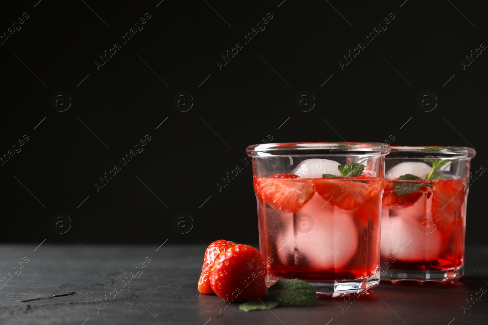 Photo of Delicious cocktails with strawberries, mint and ice balls on black table, space for text
