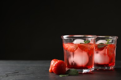 Photo of Delicious cocktails with strawberries, mint and ice balls on black table, space for text