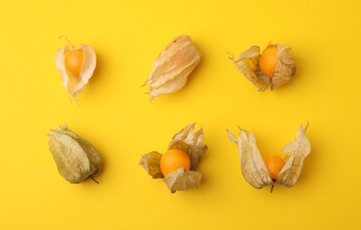 Ripe physalis fruits with calyxes on yellow background, flat lay