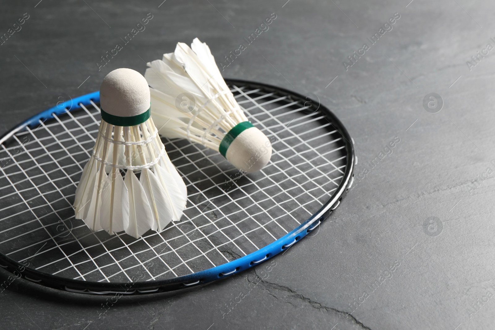 Photo of Feather badminton shuttlecocks and racket on grey textured table, closeup. Space for text