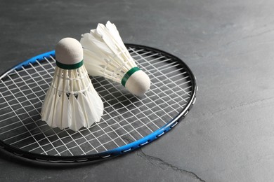 Photo of Feather badminton shuttlecocks and racket on grey textured table, closeup. Space for text