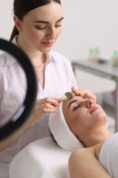 Photo of Cosmetologist making face massage with roller to client in clinic