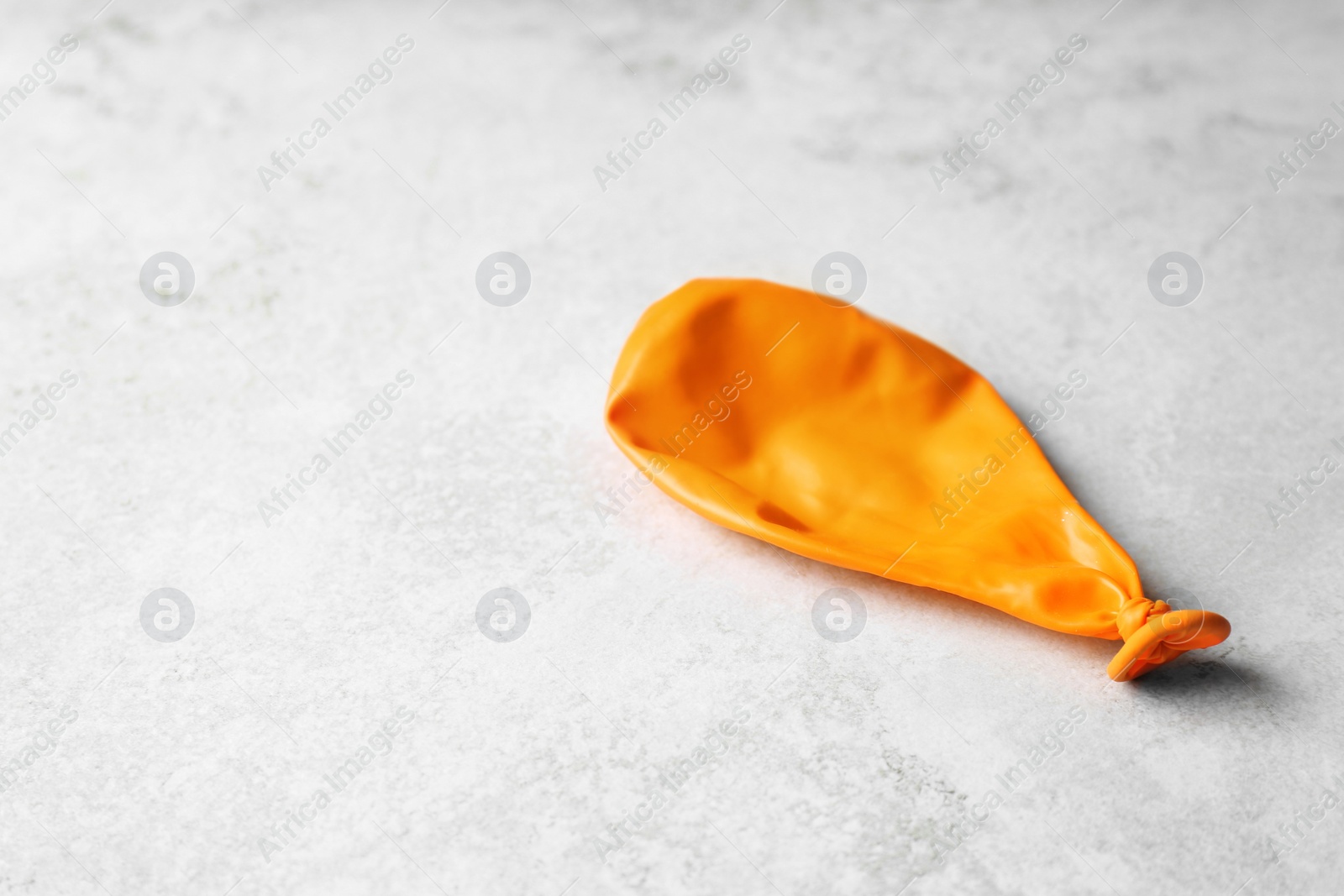 Photo of Orange deflated balloon on grey background, space for text