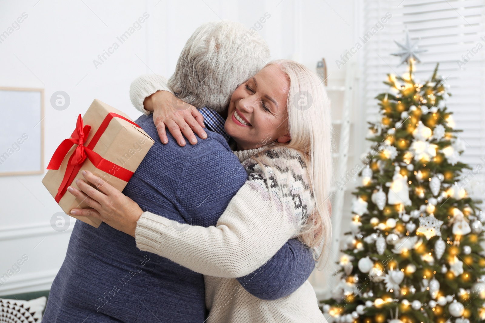 Photo of Happy mature couple with gift box hugging at home. Christmas celebration