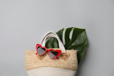 Stylish straw bag and sunglasses on grey background, flat lay with space for text. Summer accessories