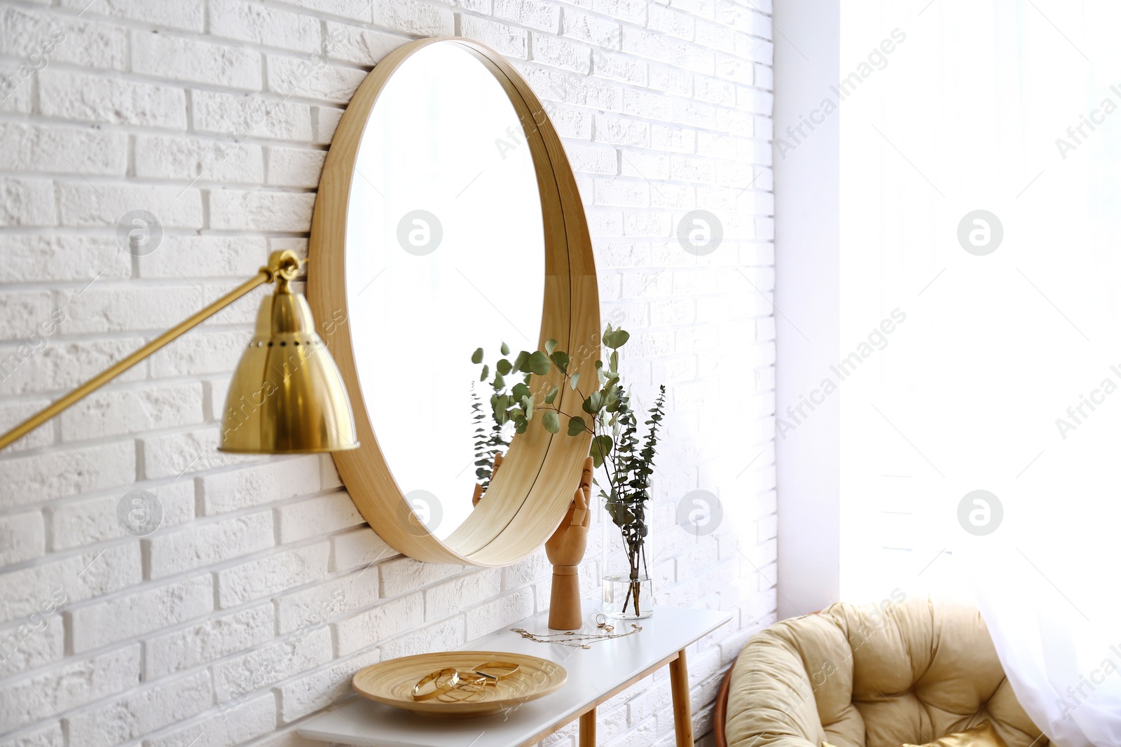 Photo of Big round mirror, table with jewelry and decor near brick wall in hallway interior. Space for text