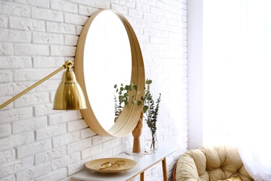 Photo of Big round mirror, table with jewelry and decor near brick wall in hallway interior. Space for text