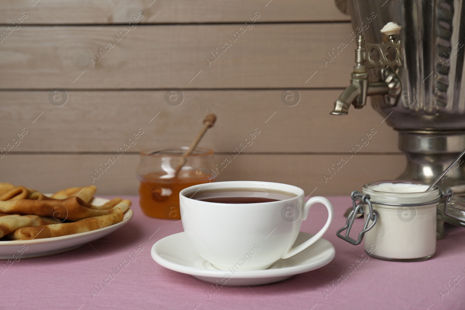 Photo of Vintage samovar, cup of hot drink and snacks served on table. Traditional Russian tea ceremony